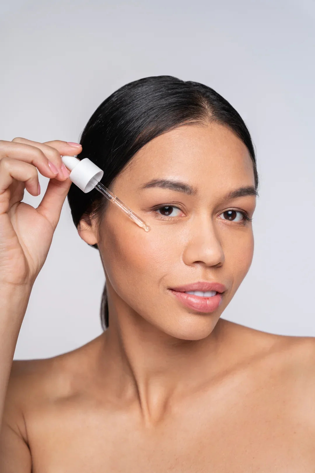 "Close-up of a person using a glycolic acid serum dropper on the cheek for acne and exfoliation."